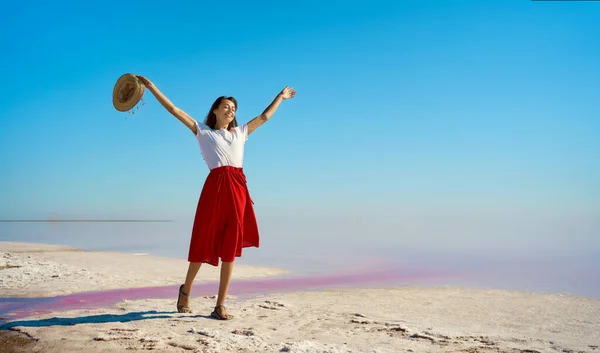 Elegant reisende kvinne lykkelig på lyse rosa sjøsaltflater, jente med hendene i været – stockfoto