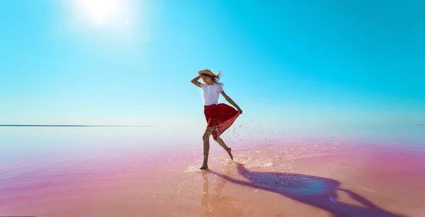 Nainen turisti kävely kirkas vaaleanpunainen vesi, rauhallinen veden pinta järven ja sininen taivas — kuvapankkivalokuva