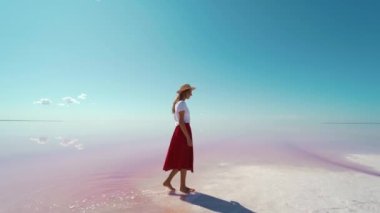 Kırmızı etekli ve şapkalı turist. Pembe gölün kıyısında, tuz düzlüklerinde yürüyor.