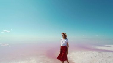 Kırmızı etekli ve hasır şapkalı bir turist. Pembe gölde yaz tatilinin tadını çıkarıyor. Tuz düzlüklerinde yürüyor.