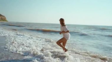 Mutlu bir kadın, deniz kıyısında zıplarken ve yatarken eğlenirken, refah ve özgürlük hissederken.