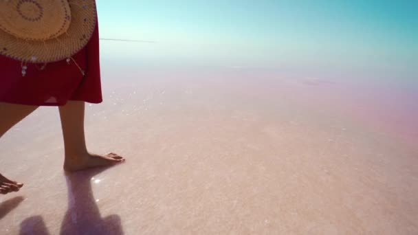 Жіночі ноги в червоній спідниці, що йде на солоному білому пляжі, тримає солом'яний капелюх — стокове відео