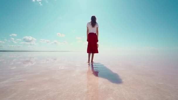 Parlak pembe sularda yürüyen kadın turist, gölün sakin su yüzeyi ve mavi gökyüzü — Stok video