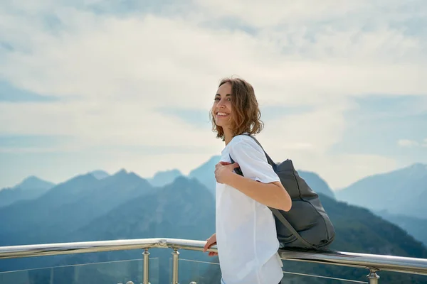 En positiv kvinnelig turist som nyter frisk luft på utsiktspunktet blant fjellene. Eventyr og reiser – stockfoto
