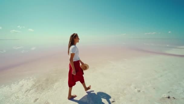Élégante jolie voyageuse heureuse sur des plats de sel de lac rose vif, fille portant une longue jupe rouge avec un chapeau de paille à la main — Video