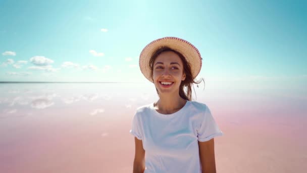Léto barevné venku portrét atraktivní usmívající se žena v klobouku šťastný pohled na kameru na růžové jezero a blu nebe přírodní pozadí — Stock video
