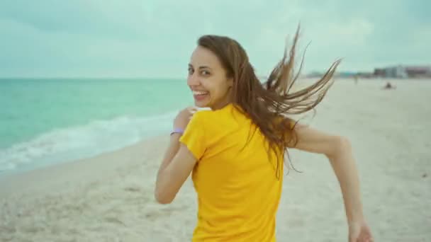 Portret gelukkige vrouw met blazen haar plezier op het strand loopt langs de kustlijn — Stockvideo