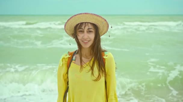 Camera zoomen closeup portret gelukkig jonge vrouw in hoed genieten van zee strand uitje vakantie, goed gevoel op winderige dag aan de kust met golven — Stockvideo