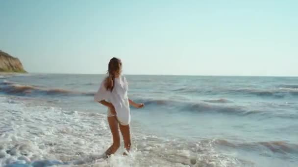 Feliz mujer alegre que se divierte al saltar y acostarse con las olas del mar en la orilla del mar, sensación de bienestar y libertad — Vídeos de Stock