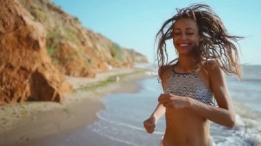 Bikinili neşeli fitness kızının yüksek dikenli kil sahilde kumsalda koşuşunun yavaş çekim görüntüleri. ss konsepti