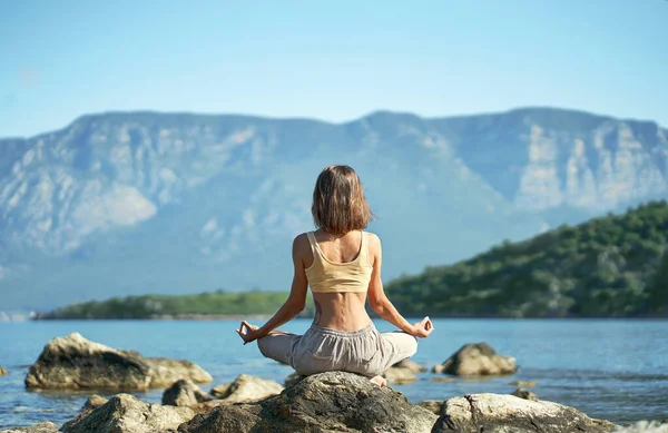 Vista trasera mujer practica yoga y meditación en playa increíble entre montañas — Foto de Stock