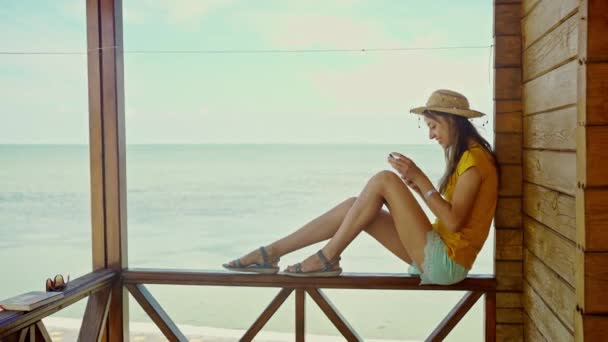 Vista lateral de la mujer en el sombrero en la playa con el ordenador portátil, el uso de teléfono inteligente, chat en línea, navegación por Internet — Vídeos de Stock