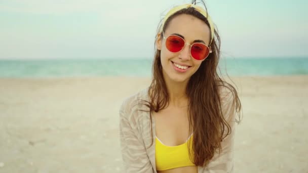 Primer plano retrato de moda al aire libre mujer joven con bikini amarillo y gafas de sol de color rosa por mar en la playa tropical — Vídeos de Stock