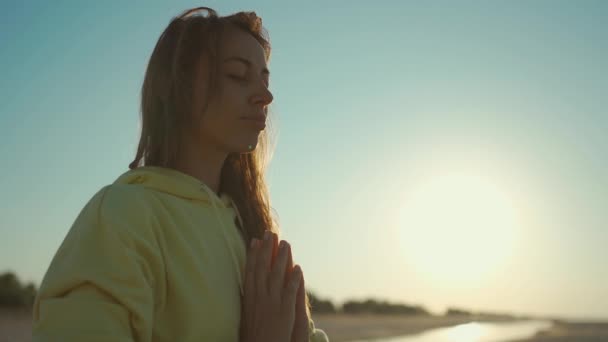 Камера движется вокруг молодой расслабленной женщины Практикуется правильное дыхание и йога медитации практикуя на красивом спокойном пляже на восходе солнца — стоковое видео