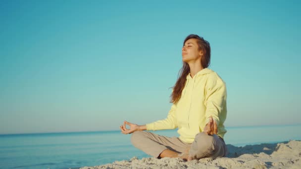 4K beautiful girl in yellow hoodie doing yoga on beautiful calm sea beach at sunrise — Stock Video