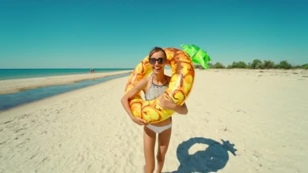 Alegre hermosa joven milenaria corriendo en la playa de arena soleada vacía sosteniendo flotador inflable amarillo de la piña en verano. — Vídeos de Stock