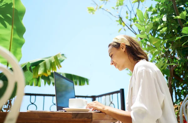 Nuori nainen liikenainen käyttää kannettavaa tietokonetta terassilla palmuja, kauko verkossa työskentely — kuvapankkivalokuva
