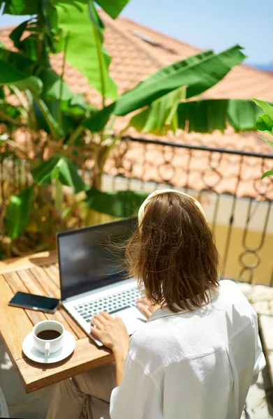 Nainen työskentelee etätyönä kannettavalla tietokoneella istuessaan parvekehotellissa — kuvapankkivalokuva