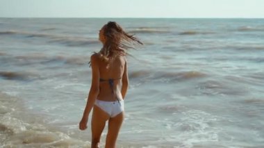 Bikini giyen, rüzgarın ve dalgaların tadını çıkartan güzel, neşeli, ince vücutlu kadının yavaş hareketi..