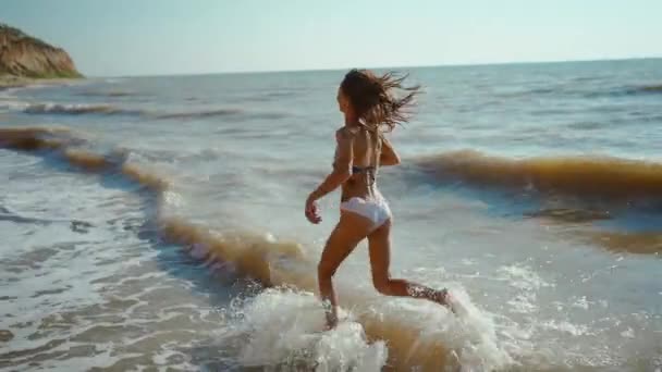Glad bekymmerslös smal kvinna med vacker passform löper längs stranden av havet med vågor efter storm, flicka jogga och hoppa genom vågor — Stockvideo