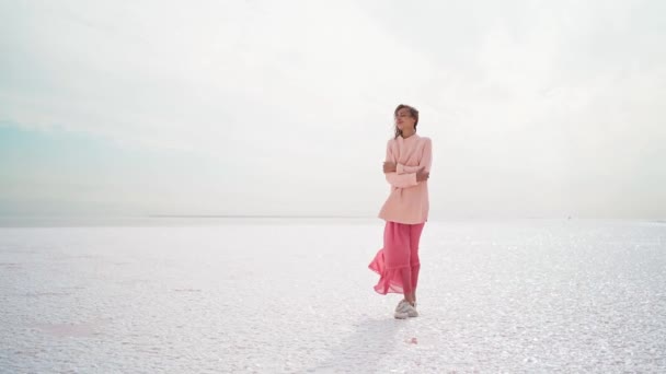 Wunderbare verträumte Frau in dickem Pullover und rosa Kleid posiert an windiger Salzküste am rosa Salzsee. — Stockvideo