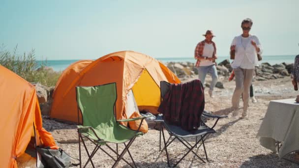 Vreugdevolle vrienden op de picknick die terugkeren van wandelingen naar de camping, speels zitten bij de campstoelen, koud bier drinken en lachen — Stockvideo