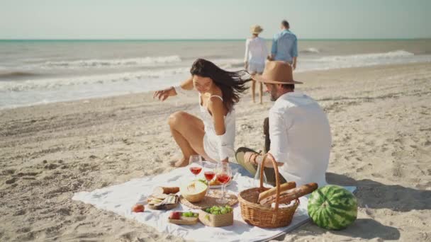 Mooi stijlvol jong familie paar gelukkig man en vrouw zitten op gezellige picknick deken. mooi mooi paar met romantische date met vrienden aan zee — Stockvideo
