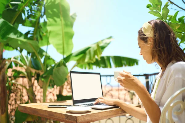 Young business woman drinking coffee and looking at laptop while sitting at balcony resort hotel — Stock fotografie