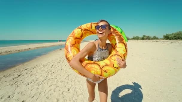 Alegre hermosa joven milenaria corriendo en la playa de arena soleada vacía sosteniendo flotador inflable amarillo de la piña en verano. — Vídeos de Stock