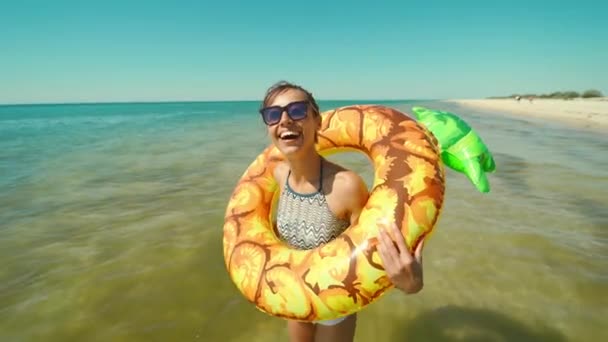 Retrato de feliz joven sonriente en gafas de sol con piña inflable de pie en agua de mar y riendo. — Vídeos de Stock