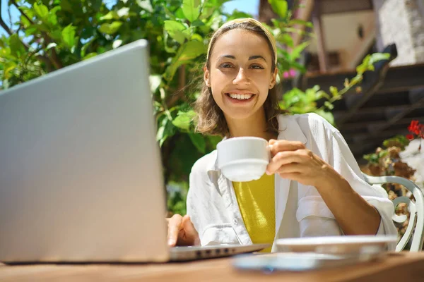 Sommerportrettkvinne som drikker kaffe og jobber med laptop på utendørs kafe – stockfoto