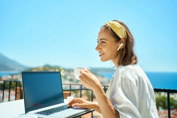 Young business woman drinking coffee and working on laptop computer at sea resort — kuvapankkivalokuva