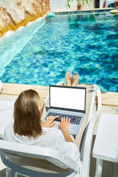 Taustakuva nainen työskentelee etänä kannettavan tietokoneen, makaa aurinkotuoleja uima-altaalla — kuvapankkivalokuva