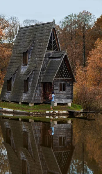 Fille voyageur debout près de la vieille maison en bois au bord du lac parmi les arbres au feuillage rouge — Photo