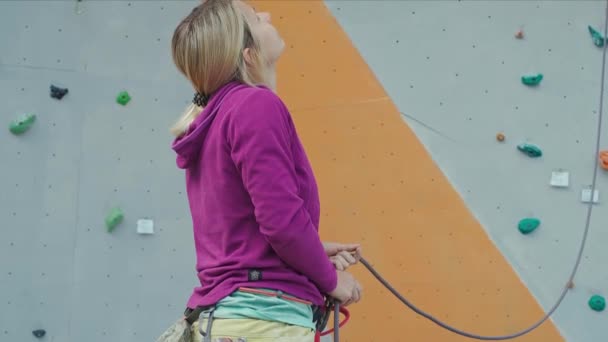 Woman rock climber in yellow pants belay with belaying device on rope in climbing gym. — Stock Video