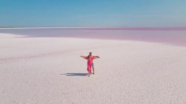Çember drone uçuşu ve pembe elbiseli mutlu romantik çiftin havadan görünüşü maden gölünün beyaz, tuzlu kıyısında duruyor. Adam şefkatle kadını kucaklıyor ve öpüyor.. 