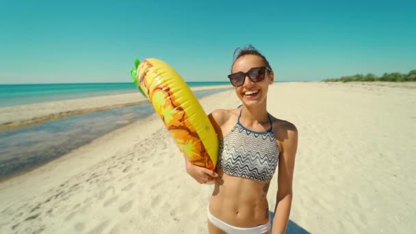 Vidám, gyönyörű, fiatal évezredes nő az üres napos homokos strandon, kezében sárga felfújható ananász úszó nyáron. — Stock videók