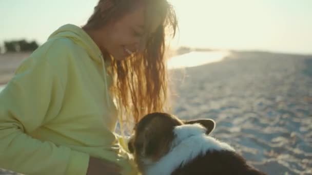 Белая женщина ласкает собаку, отдыхая утром на песчаном пляже — стоковое видео