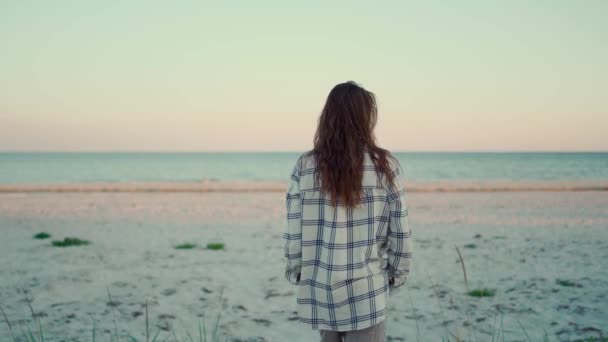 Vrouw hipster loopt op wilde zee zand strand bij zonsondergang en raakt piek van gras met de hand. vrije tijd buitenvakantie, ontsnappen aan de natuur, camping levensstijl — Stockvideo