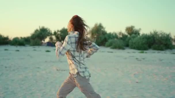 Portrait en plein air de heureuse femme mixte attrayante appréciant la promenade sur la plage de sable de mer sauvage au coucher du soleil avec belle lueur de soleil dans les cheveux — Video