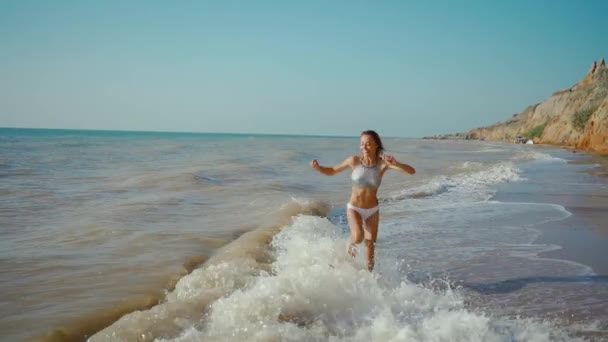 Heureux insouciante femme mince avec belle fitbody courir le long du bord de mer de la mer avec des vagues après la tempête, jogging fille et sauter à travers les vagues — Video