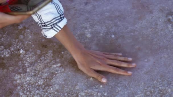 Ženy ruku na mělké vodní pobřeží růžové solné minerální jezero. dívka dotýká rukou vody a krystalizované slané dno jezera — Stock video