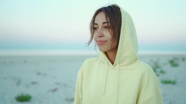 Närbild porträtt med handhållen kamera av vacker uppriktig fridfull lycklig kvinna i gul luvtröja på vacker lugn havsstrand vid soluppgången — Stockvideo