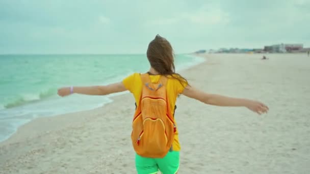 Щаслива експресія жінка з дме волоссям в жовтій футболці, що йде і розважається на океанічному пляжі, піднімаючи руки . — стокове відео