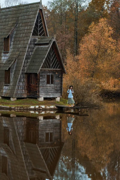 Ancienne cabane en bois au bord du lac au milieu de la forêt d'automne, femme marchant sur une jetée en bois — Photo