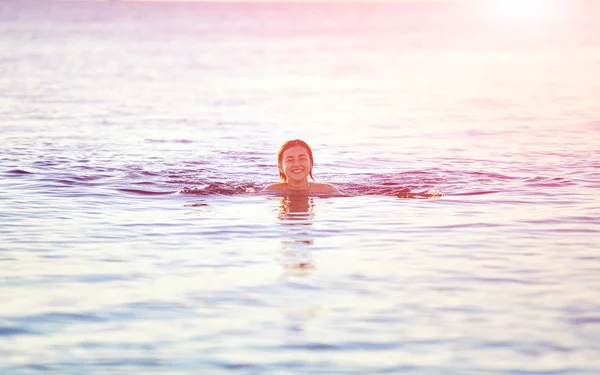 Hymyilevä tyttö ui meressä aamunkoitteessa — kuvapankkivalokuva
