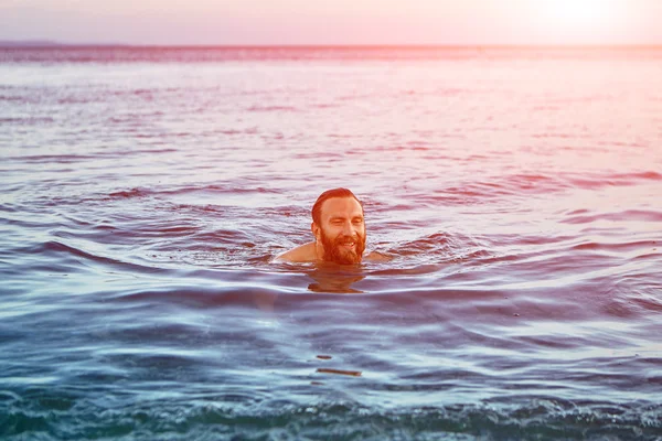Glimlachende man zwemt in de zee bij zonsopgang — Stockfoto