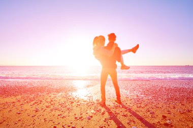 Mutlu çekici erkek ve kadın mavi gökyüzünde güneşli sahilde yürüyorlar. Bir kadını ellerinden tutan bir adam..