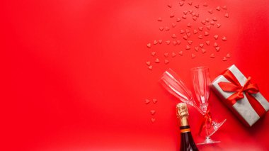 Sevgililer Günü geçmişi. Hediye kutusu, kırmızı kalpler, kırmızı şampanya ve kırmızı arka planda iki bardak. Düz konum, üst görünüm, kopyalama alanı. Banne.