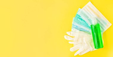 El hijyeni için koronavirüs önleyici antibakteriyel jel, sarı arka planda tıbbi cerrahi maskeler ve eldivenler. Kavram - korona virüsü koruması. Pankart. Metnin için alanı kopyala. Üst Manzara. Düz la